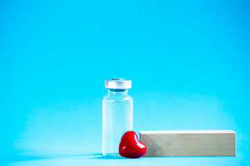 Safe vaccination concept. Glass vial with red heart on blue background.