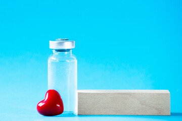 Safe vaccination concept. Glass vial with red heart on blue background.