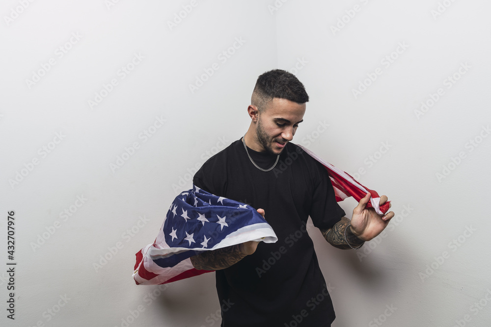 Sticker young spanish male with tattooed arms posing with an american flag isolated on a white background