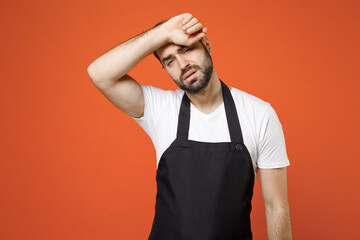 Young sick ill tired man barista bartender barman employee in black apron white t-shirt work in coffee put hand on forehead having headache isolated on orange background studio Small business startup.