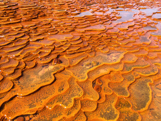 Detail of sediments in orange mineral pool of natural water spring in Damia with stream or rising spring to the air