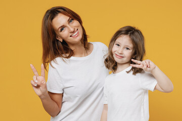 Happy woman in white t-shirt have fun with cute child baby girl 5-6 years old show v-sign. Mommy little kid daughter isolated on yellow orange color background studio Mother's Day love family concept