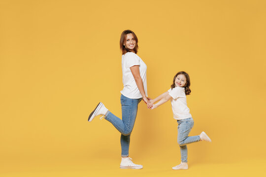 Full Length Happy Woman In Basic White T-shirt Have Fun With Cute Child Baby Girl 5-6 Years Old Hold Hands. Mom Little Kid Daughter Isolated On Yellow Color Background Studio Mother's Day Love Family