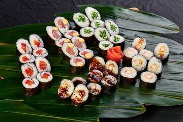 sushi set with tuna, salmon, shrimp, eel and color cucumber lies on a background of green bamboo leaves on a black background