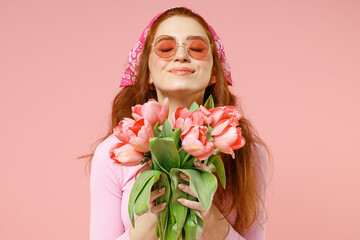 Young smiling trendy satisfied woman with closed eyes wearing rose clothes bandana glasses hold...