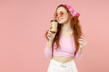 Young smiling happy woman 20s wearing rose clothes bandana glasses holding paper cup of coffee drink hot tea with closed eyes isolated on pastel pink color background studio People lifestyle concept.