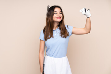 Young caucasian woman isolated on beige background playing golf and celebrating a victory