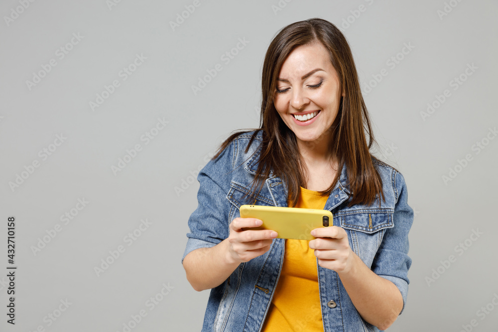 Wall mural young gambling woman wear in denim jacket yellow t-shirt using play racing on mobile cell phone hold