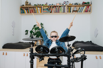 Little boy superstar in sunglasses playing electronic drums at home