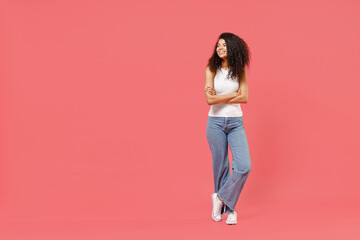 Fototapeta na wymiar Full length young fun smiling happy friendly positive african american woman 20s wearing white tank shirt hold hands crossed folded look aside isolated on pink background. People lifestyle concept
