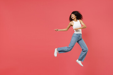 Fototapeta na wymiar Full length young fun happy positive african american woman in casual white tank shirt jump high point index fingers aside on workspace area mock up isolated on pink color background studio portrait.
