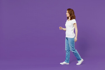 Fototapeta na wymiar Full length side view young smiling happy cheerful friendly caucasian woman 20s wear white basic casual t-shirt jeans walking going look aside isolated on dark violet color background studio portrait