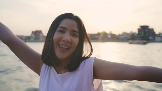 Happy young Asian woman blogger tourist with casual style looking at camera take selfie video call enjoy with beautiful sunset river view cafe in city town, Lifestyle tourist travel holiday concept.