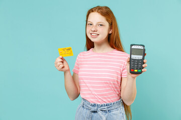 Little redhead kid girl 12-13 year old in pink t-shirt hold wireless modern bank payment terminal process acquire credit card payments isolated on pastel blue background Lifestyle children concept