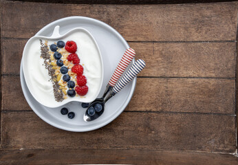 Serving of Yogurt with Whole Fresh Blueberries, Raspberries and Chia Seeds on Rustic Wooden Table.