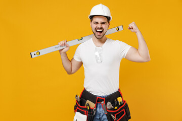 Young employee handyman man in protective helmet hardhat hold build bubble spirit level do winner gesture isolated on yellow background Instrument accessories renovation apartment room Repair concept.