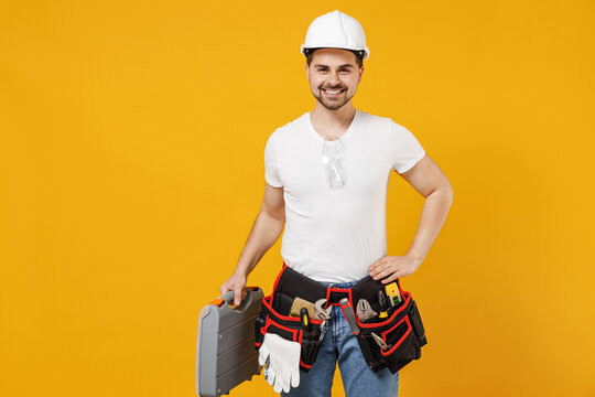 Young confident employee handyman man 20s in protective helmet hardhat tool case box stand akimbo isolated on yellow background Instruments accessories renovation apartment room Repair home concept. - Powered by Adobe