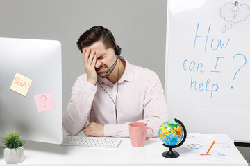 Employee operator business man in set microphone headset for helpline assistance sit work at call center office desk with pc computer do facepalm epic fail gesture isolated on grey background studio.