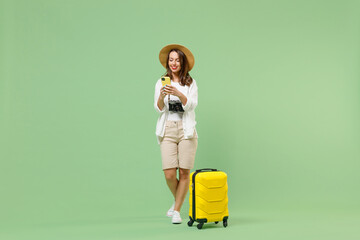Full length traveler tourist woman in casual clothes hat hold suitcase mobile cell phone booking taxi hotel isolated on green background Passenger travel abroad weekends Air flight journey concept.