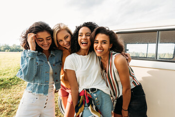 Young laughing women standing at van having good times during summer vacation