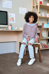 Happy smiling African American black pupil with afro hair sitting on chair near the desk with...