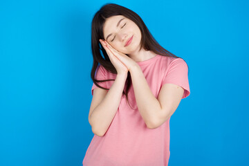 young beautiful Caucasian woman wearing pink T-shirt over blue wall sleeping tired dreaming and posing with hands together while smiling with closed eyes.