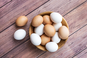 Wooden bowl with brown and white chicken eggs on wood table. Brown and white eggs in bowl on wood background. Free-range organic eggs. Healthy food concept. - Top view
