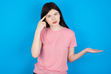young beautiful Caucasian woman wearing pink T-shirt over blue wall confused and annoyed with open palm showing copy space and pointing finger to forehead. Think about it.
