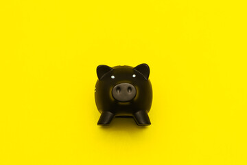 Black pig figurine on a yellow background. A piggy bank for money in the shape of a pig. A piggy bank animal.