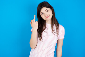 Fototapeta premium young beautiful Caucasian woman wearing stripped T-shirt over blue wall shows middle finger bad sign asks not to bother. Provocation and rude attitude.