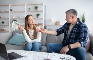 Mature woman with fan of dollars and her husband asking for money during family budget planning, indoors
