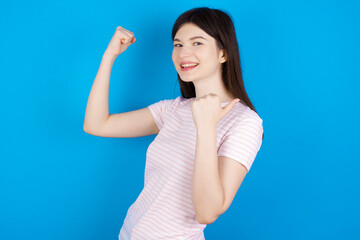 Hooray cool young beautiful Caucasian woman wearing stripped T-shirt over blue wall point back empty space hand fist