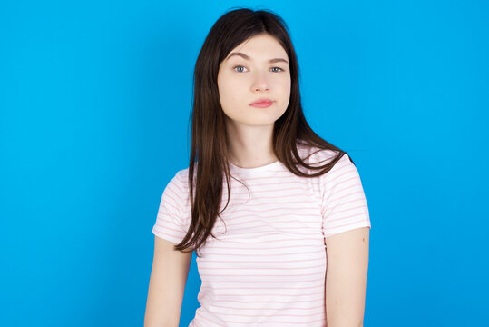 Displeased young beautiful Caucasian woman wearing stripped T-shirt over blue wall frowns face feels unhappy has some problems. Negative emotions and feelings concept