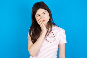 young beautiful Caucasian woman wearing stripped T-shirt over blue wall with toothache