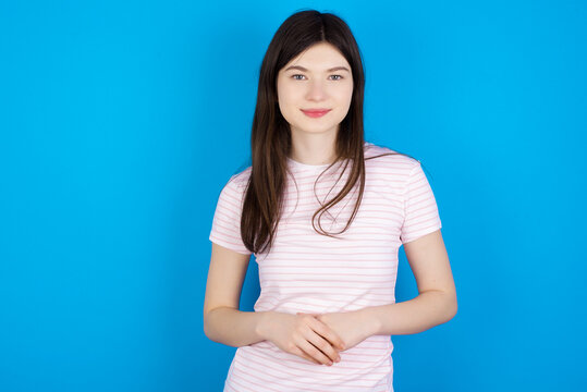 Photo of cheerful confident young beautiful Caucasian woman wearing stripped T-shirt over blue wall arms together