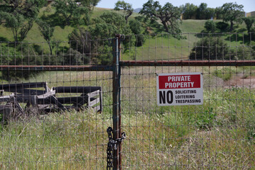 Red white black sign on a rural fence gate saying PRIVATE PROPERTY NO SOLICITING NO LOITERING NO...