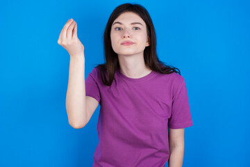 young beautiful Caucasian woman wearing purple T-shirt over blue wall angry gesturing typical italian gesture with hand, looking to camera