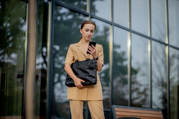 Adult Caucasian Confident Young Business Woman is Talking on Phone Outside near Modern Office Building