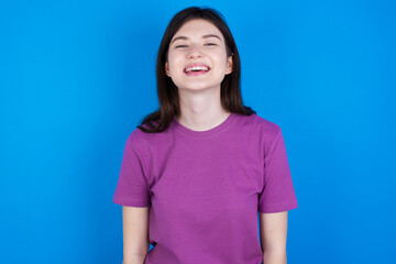young beautiful Caucasian woman wearing purple T-shirt over blue wall with a happy and cool smile on face. Lucky person.