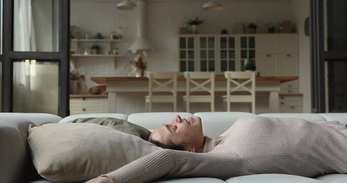Young cute inspired woman falling down on sofa stretched arms looking happy after romantic date feels fall in love. Female enjoy stress-free day off, full of energy and positive relaxing alone at home