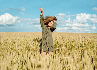 young girl is dancing in a wheat field. Runs his hand over ears. Stands with his back. Hair flying in the wind, life style. emotionally spinning and jumping. freedom concept and hot summer