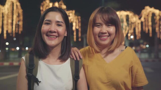 Happy young Asian girls couple tourist with casual style smiling looking at camera peaceful picture of background in city street at night. Lifestyle tourist travel holiday concept.