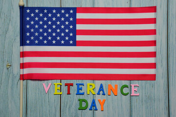 On the flag of the USA, the text VETERANCE DAY is lined with multicolored letters on a wooden background.
