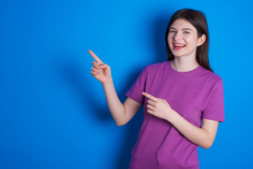 young beautiful Caucasian woman wearing purple T-shirt over blue wall point at copyspace recommend sales discounts