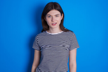 Portrait of dissatisfied young beautiful Caucasian woman wearing pink jacket over blue wall smirks...