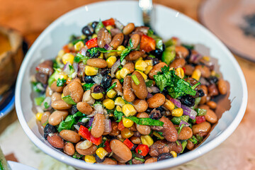 Macro closeup with texture of bean salad with cilantro, red onion, raisins, peppers and corn as dinner meal for family with bokeh background