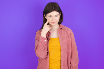 young beautiful Caucasian woman wearing blue T-shirt over blue wall, looking, observing, keeping an eye on an object in front, or watching out for something.