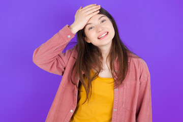 Fototapeta na wymiar Oops, what did I do? young beautiful Caucasian woman wearing casual clothes over purple wall holding hand on forehead with frightened and regret expression.