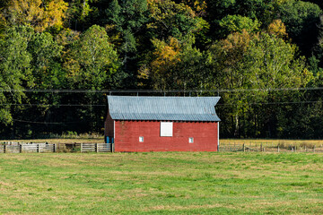 Obraz premium Shed barn with fence in autumn fall field in countryside landscape of farm farmland in West Virginia near Seneca Rocks and red house building