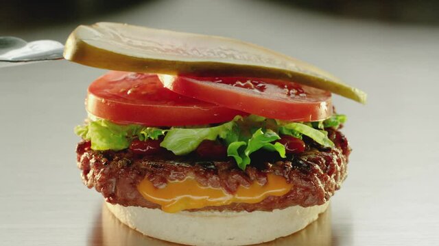 Cheese stuffed hamburger being  built with tomato lettuce and pickle